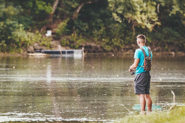 Un joven está pescando en la costa de un lago de agua dulce bordeado por un paisaje exuberante.