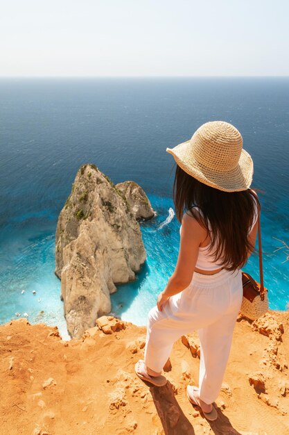 Una joven está de pie en el borde de un acantilado y mira el mar azul