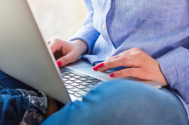 La joven está sentada en el alféizar de la ventana y trabajando en la computadora portátil