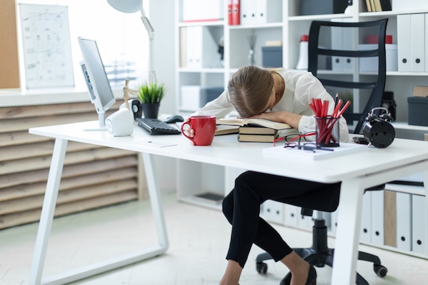 Una joven está sentada en una mesa en la oficina. La niña puso la cabeza sobre el libro abierto.