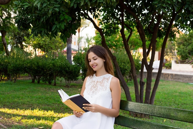 La joven está sentada en el parque y disfruta leyendo un libro