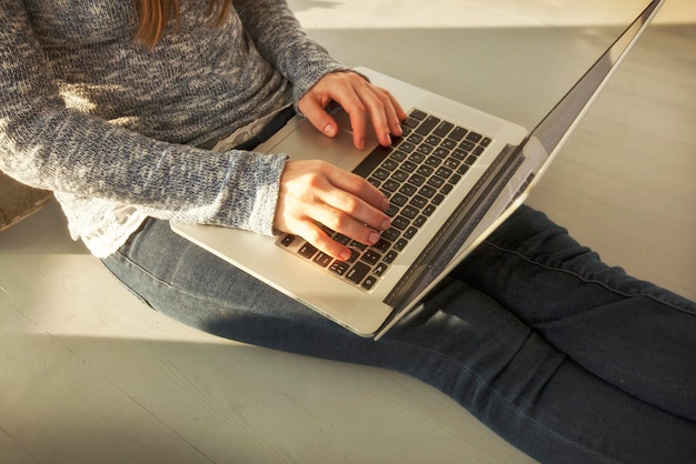 La joven está sentada en el suelo y trabaja con una computadora portátil