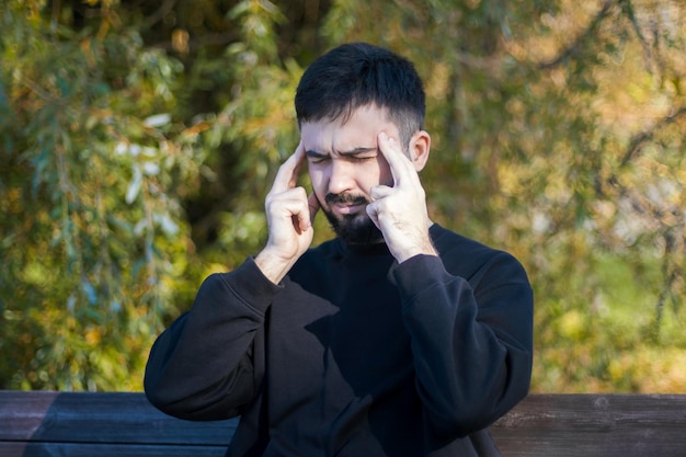 El joven está sentado en el parque y meditando. Intenta concentrarse en los pensamientos. tambien tiene dolor de cabeza