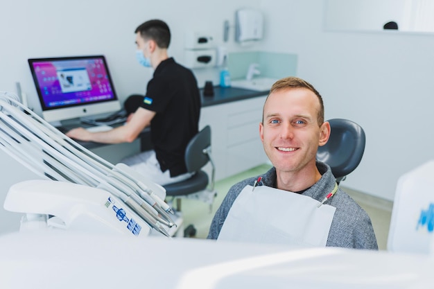 Un joven está sentado en una silla dental y un dentista está trabajando en una computadora Cita con el dentista