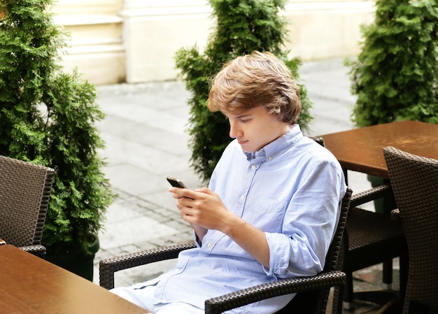 Un joven está sentado en una silla mirando su teléfono.