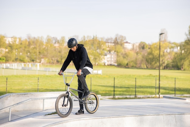 Un joven está en un skatepark en una rampa sosteniendo una bicicleta bmx con un pie en el pedal