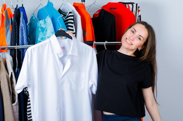 La joven está sonriendo sosteniendo la camisa en el fondo de la ropa