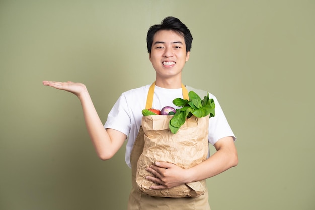 Joven está sosteniendo una bolsa llena de verduras sobre fondo blanco.