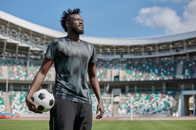 Un joven se para en un estadio con un balón de fútbol en la mano.