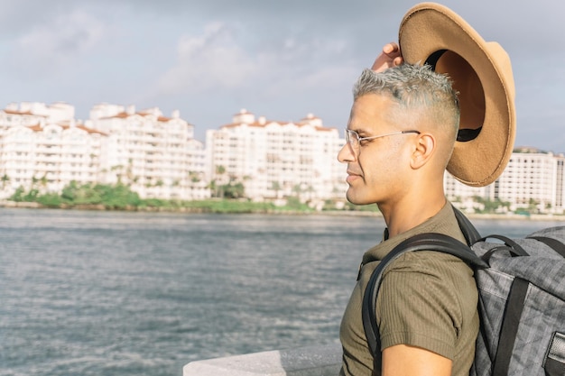 Foto joven con estilo levantando su anuncio de sombrero mirando a lo lejos en la playa