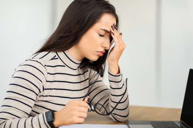 Una joven estresada en casa con dolor de cabeza sosteniendo sus gafas en una mano