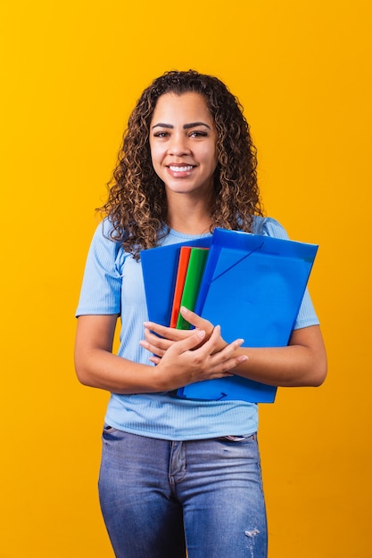 Joven estudiante adolescente afroamericano en ropa casual sosteniendo libros aislados sobre fondo amarillo retrato de estudio. Educación en el concepto de colegio universitario de secundaria. simulacro de espacio de copia. Vertical