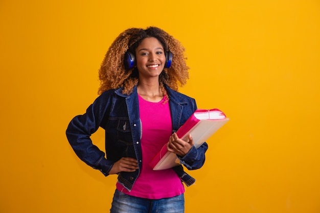 Joven estudiante afro con libros sobre fondo amarillo.