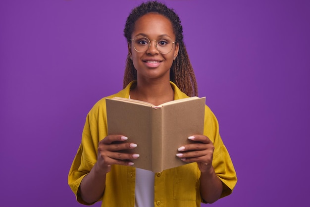 Joven estudiante afroamericana inteligente e inquisitiva sonriendo sosteniendo un libro