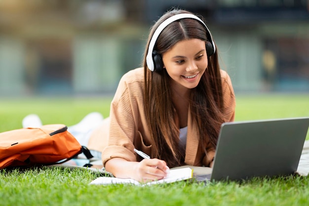 Una joven estudiante alegre asiste a una clase en línea usando una computadora portátil