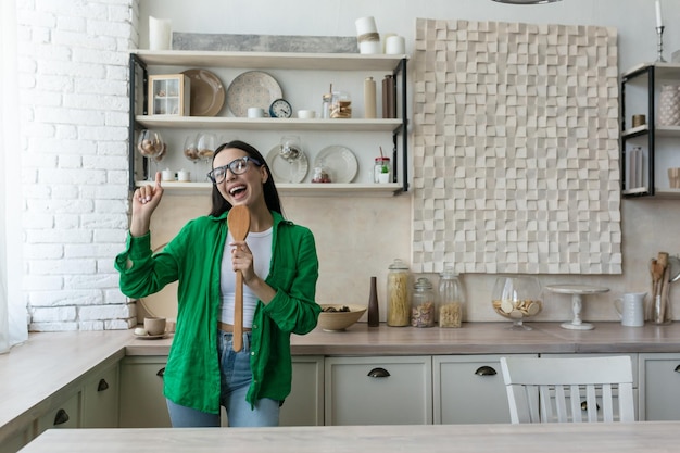 Una joven estudiante ama de casa alegre y feliz canta en la cocina en un objeto de cocina como un