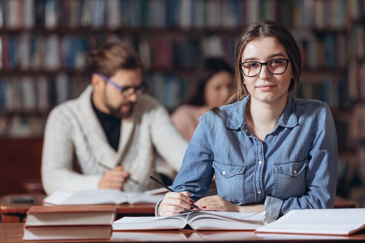 Joven estudiante con anteojos estudiando en la biblioteca universitaria