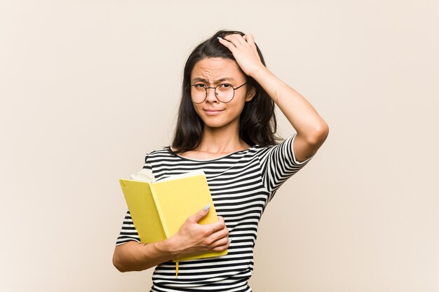 Joven estudiante asiática con un libro sorprendido, ha recordado una reunión importante.