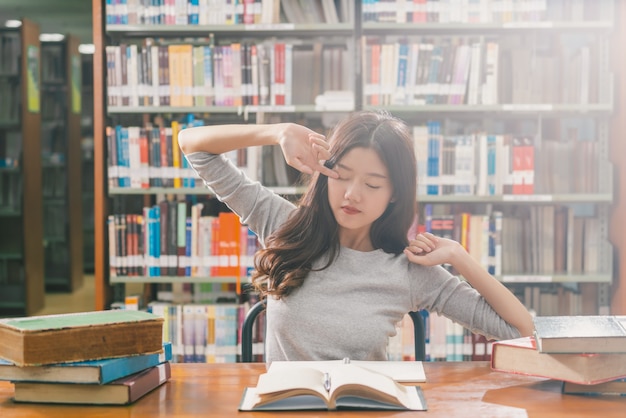 Joven estudiante asiática en traje casual leyendo y haciendo estiramiento en la biblioteca de la universidad