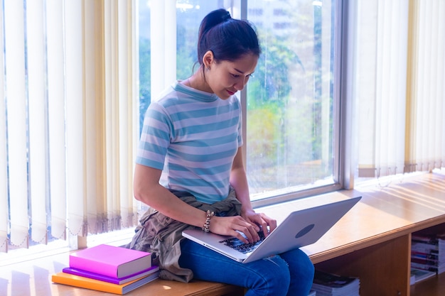 Una joven estudiante asiática usa una computadora portátil en la biblioteca.