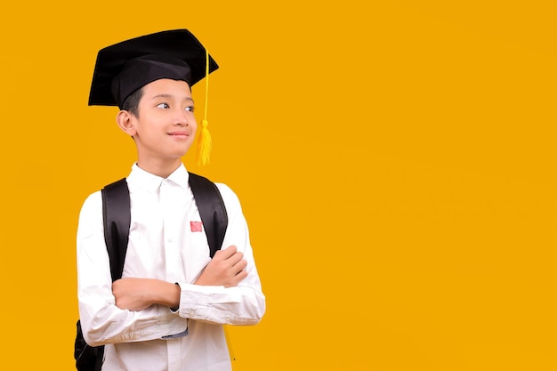 Joven estudiante asiático con mochila y gorra de graduación brazos cruzados mientras mira hacia el lado