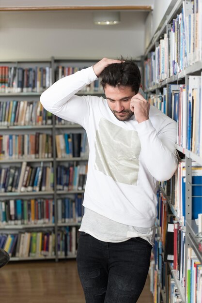 Joven estudiante barbudo hablando por teléfono mientras se prepara para los exámenes en la biblioteca de Univercity