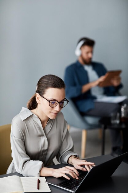 Joven estudiante bonita escribiendo mientras está sentada en el escritorio frente a la computadora portátil