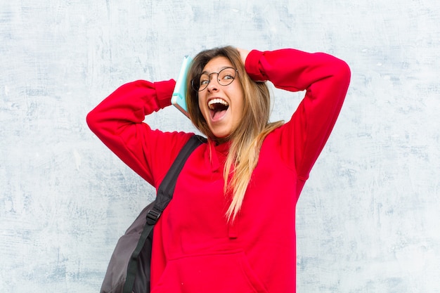 Joven estudiante bonita levantando las manos a la cabeza, con la boca abierta, sintiéndose extremadamente afortunado, sorprendido, emocionado y feliz