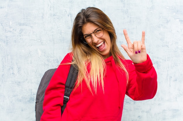 Joven estudiante bonita que se siente feliz, divertida, segura, positiva y rebelde, haciendo letrero de rock o heavy metal con la mano