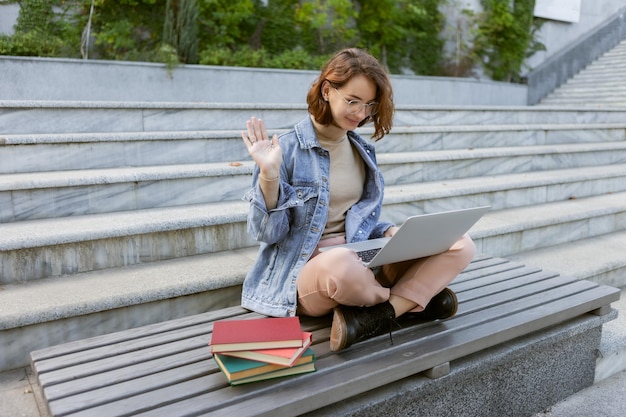 Una joven estudiante bonita sentada con una laptop Una chica caucásica tiene una llamada en línea al aire libre