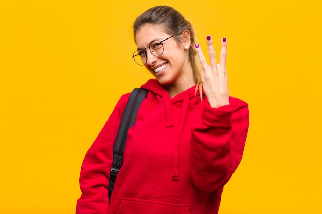 Joven estudiante bonita sonriendo y mirando amistosamente, mostrando el número tres o tercero con la mano hacia adelante, contando hacia atrás