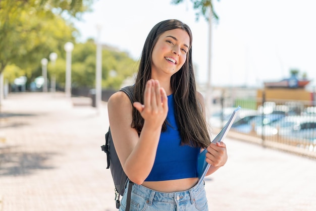 Joven estudiante brasileña al aire libre invitando a venir con la mano Feliz de haber venido