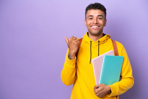 Joven estudiante brasileño aislado de fondo morado apuntando hacia un lado para presentar un producto