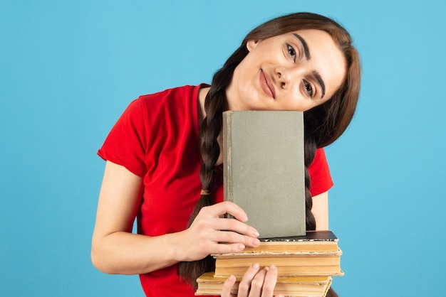 Joven estudiante en camiseta roja con libros de pie sobre la pared azul.