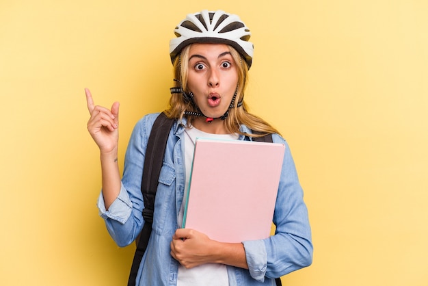 Joven estudiante caucásica mujer vistiendo un casco de bicicleta aislado sobre fondo amarillo apuntando hacia el lado