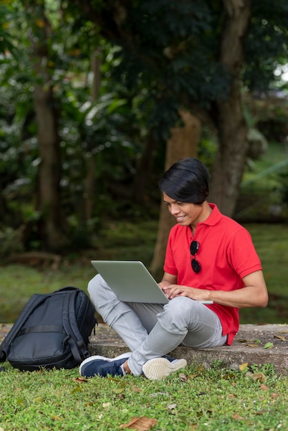 Joven estudiante en el césped del parque se sienta debajo de un árbol y trabaja con un portátil Panamá