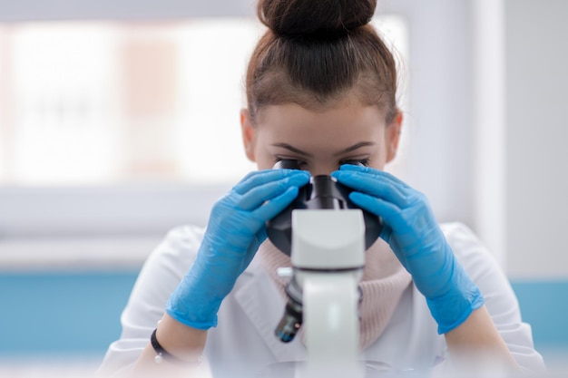 Joven estudiante científica mirando a través de un microscopio mientras investiga en el laboratorio