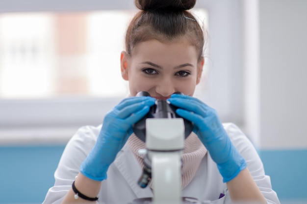 Joven estudiante científica mirando a través de un microscopio mientras investiga en el laboratorio