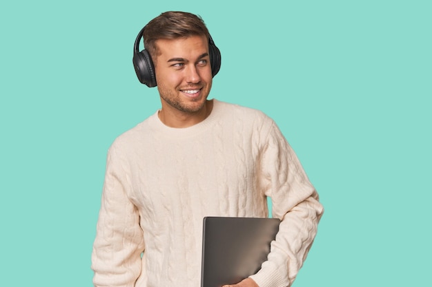 Joven estudiante con una computadora portátil mira a un lado sonriendo alegre y agradable