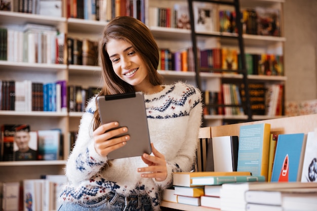 Joven estudiante enfocada usando una tableta en una biblioteca