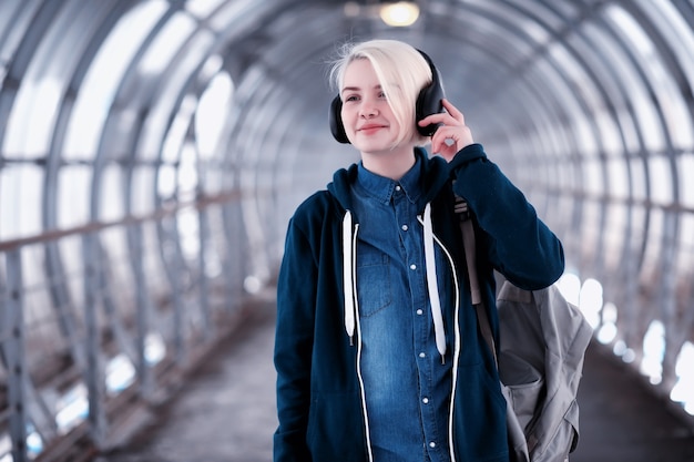 Joven estudiante escuchando música en grandes auriculares en el túnel del metro