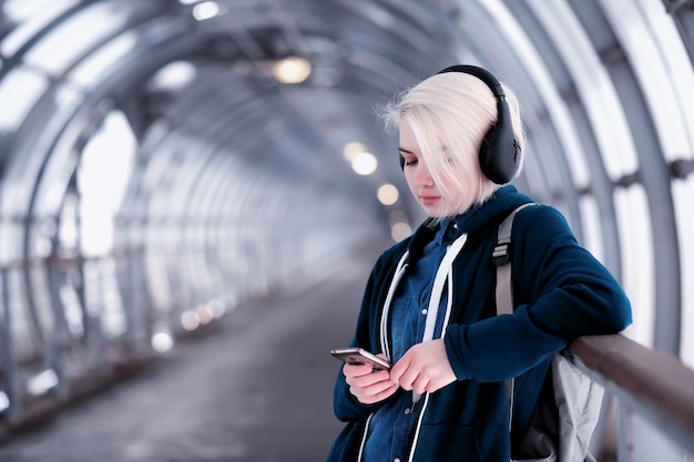 Joven estudiante escuchando música en grandes auriculares en el túnel del metro