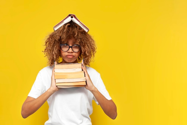 joven estudiante estadounidense rizada cansada con gafas sostiene libros en fondo aislado amarillo