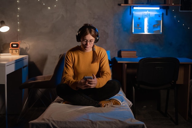 Una joven estudiante estudia sentada en la cama en el dormitorio usando un teléfono inteligente Una chica chateando en el teléfono móvil en el dormitorio de casa
