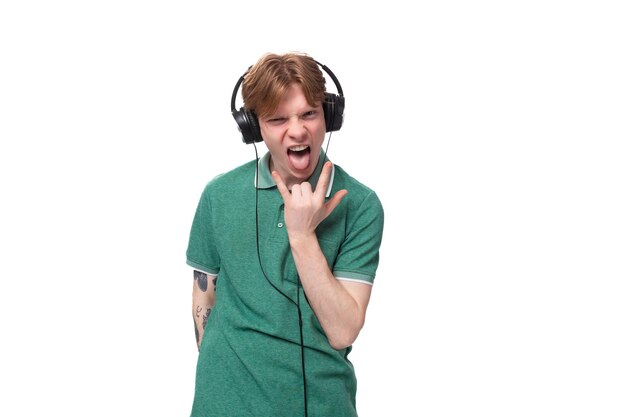 Un joven estudiante europeo, alegre y delgado, con el pelo rojo y una camiseta verde, escucha música a todo volumen