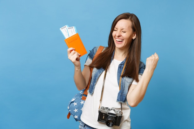 Joven estudiante feliz con cámara de fotos vintage retro con pasaporte, billetes de tarjeta de embarque haciendo gesto ganador aislado sobre fondo azul. Educación en la universidad en el extranjero. Vuelo aéreo.