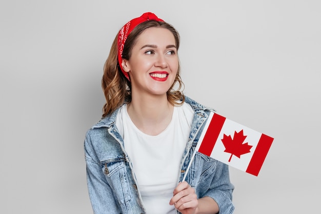 Joven estudiante feliz sonriendo y sosteniendo una pequeña bandera de Canadá y mirando a otro lado aislado sobre la pared gris, día de Canadá, día de fiesta, aniversario de la confederación, espacio de copia