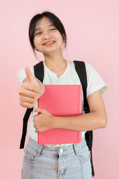 Una joven estudiante feliz sostiene un libro rosa y una mochila con fondo rosa