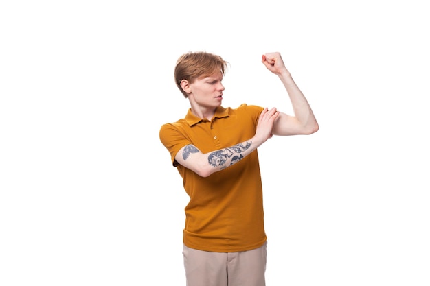 Un joven estudiante fuerte con pelo rojo y un tatuaje en el brazo lleva una camiseta amarilla