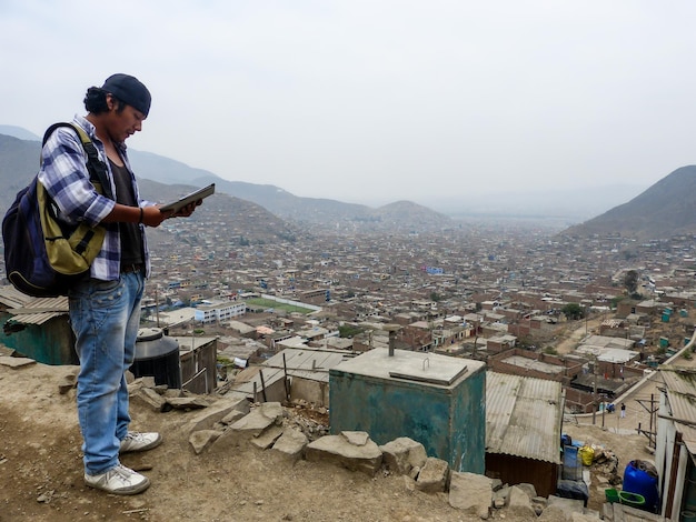 Joven estudiante con gorra y mochila en la cima de una montaña mirando un pueblo